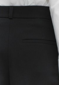 Zwarte op maat gemaakte broeken met een gladde textuur, een slim fit en een enkele achterzak. De tailleband is plat met een subtiele vouwlijn.