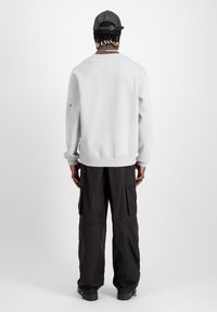 Felpa grigia chiara con polsini a costine, vestibilità comoda e etichetta sul retro. Pantaloni cargo scuri con tasche laterali e gambe dritte. Cappellino nero.