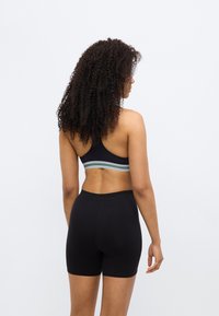 Brassière de sport noire avec une bande rayée, associée à un short noir ajusté. Texture de tissu lisse avec une coupe sportive et moulante.