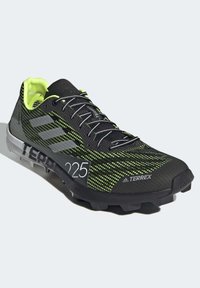 Czarno-neonowo zielony but do biegania z siateczkową cholewką, teksturowaną podeszwą i kolcami zapewniającymi przyczepność. Zawiera logo z trzema paskami i detal "225".