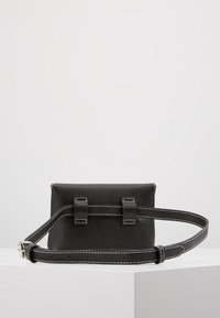 Černá kožená křížová taška s elegantním obdélníkovým tvarem, vybavená bílým prošíváním, dvěma předními popruhy a nastavitelným popruhem.