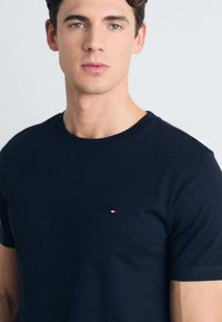Camiseta de algodón azul marino con cuello redondo y mangas cortas. Presenta un pequeño logo rojo, blanco y azul en la parte izquierda del pecho.