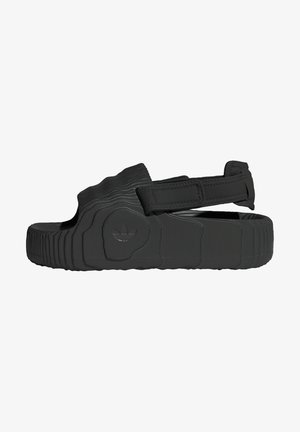 Black sandals made of textured rubber with a wide strap and adjustable velcro closure. Features a patterned sole and branded logo detail.