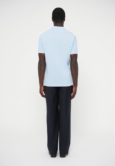 Ανοιχτό μπλε πόλο μπλουζάκι με κοντά μανίκια, συνδυασμένο με σκούρα ναυτικά παντελόνια με λεπτές ρίγες. Το σύνολο έχει άνετη εφαρμογή και λεία υφή.