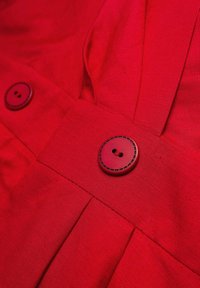 Czerwona tkanina o gładkiej fakturze ma dwa czerwone guziki z wyszywaną obwódką. Projekt zawiera szczegółowe fałdy na dole.