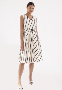 Kostium w paski bez rękawów w kremowym kolorze z czarnymi liniami, z dekoltem w kształcie litery V, dopasowaną talią z czarnym paskiem i rozkloszowaną spódnicą.