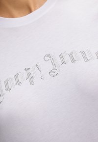 Witte katoenen t-shirt met een tekstontwerp van zilveren rhinestones, met een gladde textuur en een standaard ronde hals.