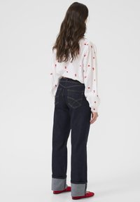 Indigo kavbojke iz jeansa s ravnimi hlačnicami in zavihanim robom, z zapletenim šivom na zadnjih žepih, združene z belo vezeno bluzo.