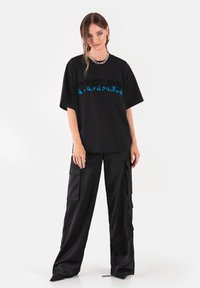 Czarny oversize t-shirt z niebieską grafiką płomieni w wyrazistym kroju czcionki. Połączony z luźnymi czarnymi spodniami cargo z bocznymi kieszeniami.