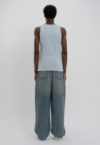 Top de alças azul claro em ribana combinado com calças de ganga desgastadas e oversized, com grandes bolsos traseiros e um corte descontraído.