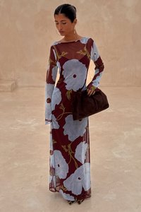 Lång vinröd klänning med stora ljusblå blommönster, genomskinligt tyg och långa ärmar. Kombinerad med en mörkbrun clutchväska.