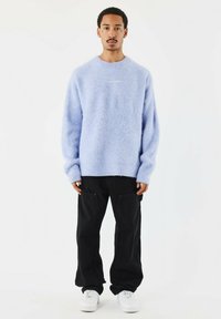 Lichtblauwe donzige trui met lange mouwen, ronde hals, gecombineerd met zwarte comfortabele broek en witte sneakers. Minimalistisch ontwerp.