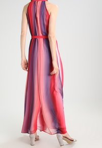 Robe maxi en tissu transparent avec un dégradé de teintes roses et violettes, présentant un col halter et une taille cintrée, assortie de talons légers.