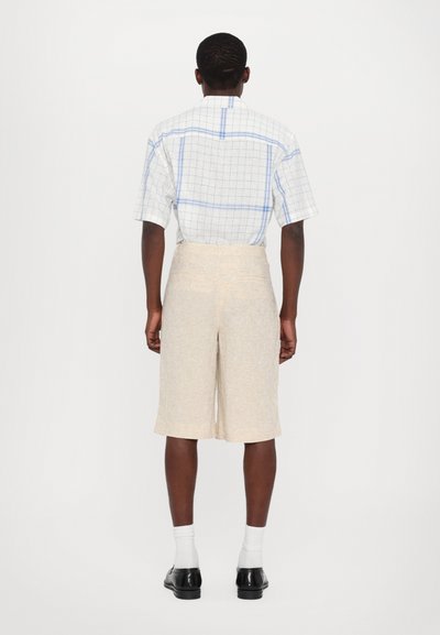 Chemise à manches courtes à carreaux bleu clair et blanc, associée à un short texturé beige. Elle dispose d'un empiècement arrière et de manches montées.