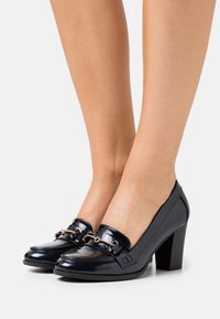 Navy modré lakované kožené lodičky na vysokém podpatku s akcentem z řetízku ve zlaté barvě, s kulatou špičkou a blokovým podpatkem.