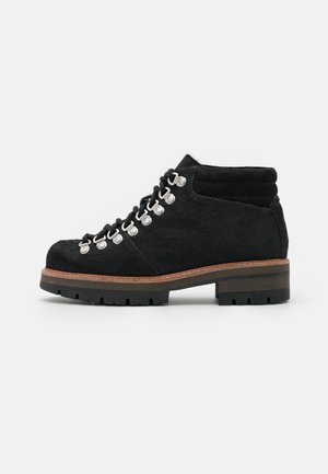Botte de randonnée en daim noir avec lacets noirs, œillets argentés, col de cheville rembourré et semelle en caoutchouc épaisse avec une bordure intermédiaire marron.