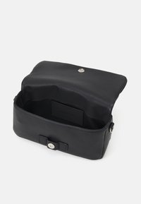 Czarna skórzana torba o smukłym prostokątnym kształcie, z zapięciem na magnes i wnęką wewnętrzną do organizacji. Gładka faktura.