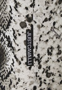 Černobílá látka s hadím vzorem a skvrnami. Na štítku je nápis "JUSTCAVALLI," zašitý na okraji.