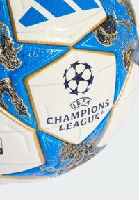 White soccer ball with blue and gold accents, featuring UEFA Champions League logo and intricate lion graphics on its surface.