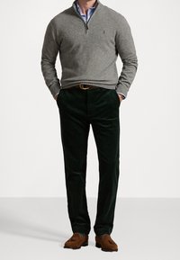 Pull-over en maille grise avec col zippé, associé à un pantalon en velours côtelé vert foncé et des mocassins marron, mettant en valeur des tissus texturés et une coupe ajustée.