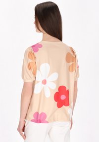 Lys beige kortærmet top med store blomster mønstre i pink, rød og orange. Glat stof med en afslappet pasform og rynkede ærmer.