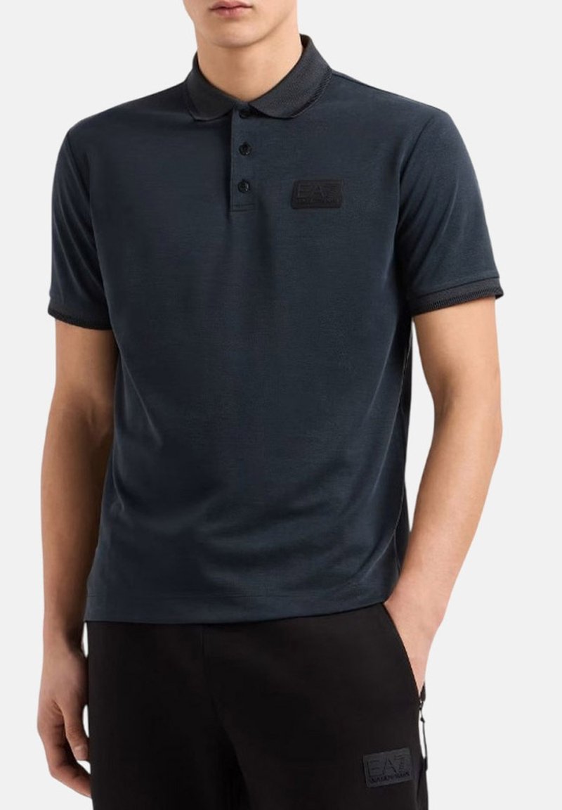 Polo a maniche corte blu navy con colletto, pattina con tre bottoni, tessuto testurizzato e una toppa con logo sul petto.