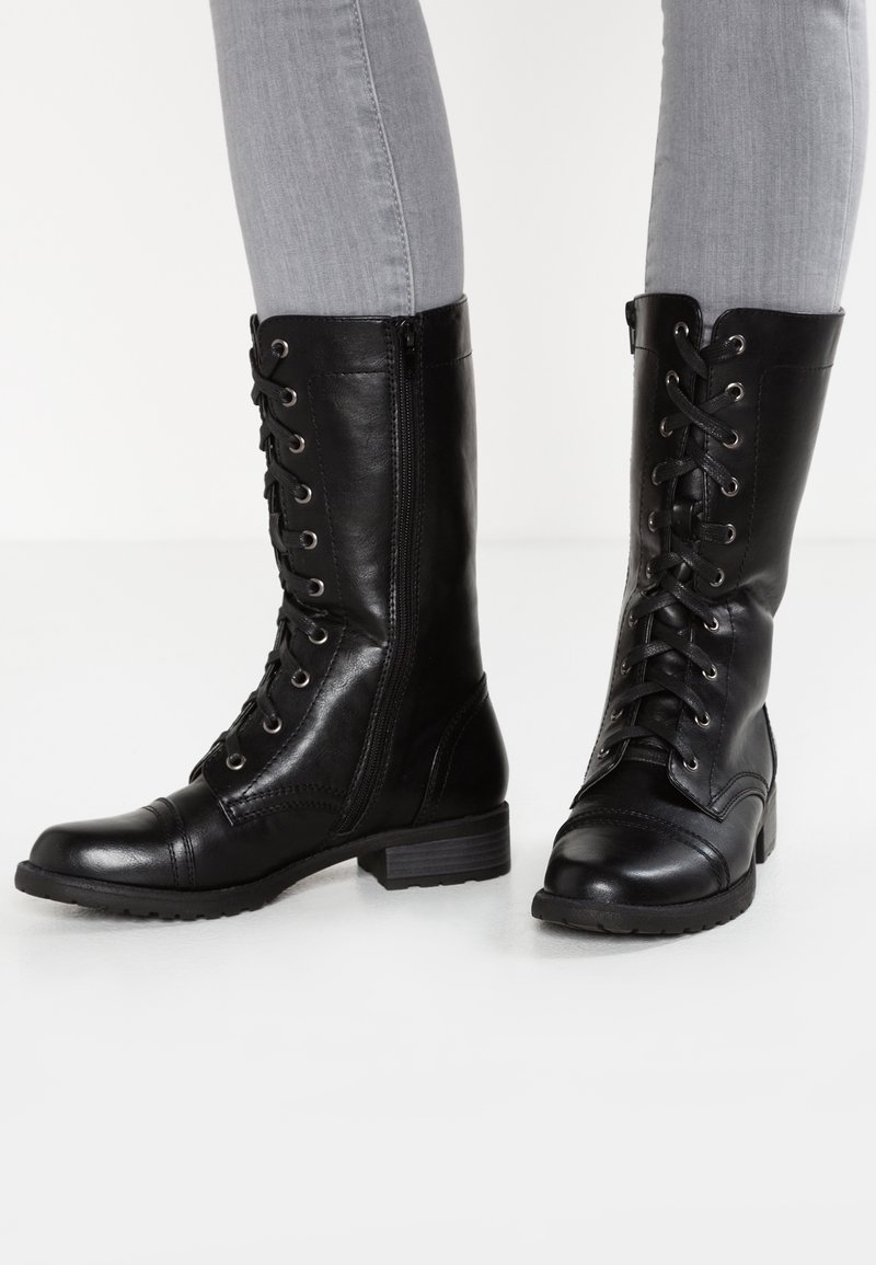 Botas de cuero negras hasta la rodilla con punta redonda, cordones en la parte frontal, cremallera lateral, acabado texturizado y tacón bajo en bloque.