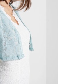 Lichtblauwe kanten sjaal die over een witte kanten jurk is gedrapeerd, met ingewikkelde bloemenpatronen en een zachte, doorschijnende textuur.