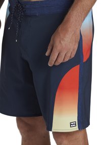 Bañadores de marinero con un panel en degradado multicolor en rojo, naranja y amarillo. Incluyen una cinturilla con cordón y un parche con el logo.