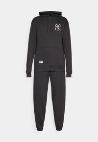 Melnas kokvilnas kapuce ar priekšējo kabatu un auklu, ar zelta Yankees logo. Apvienots ar atbilstošām pieguļošām sporta biksēm.