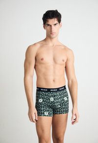 Boxershorts in dunklen Grüntönen mit großen, wiederholten "HUGO"-Texten in Schwarz und Weiß. Elastischer Taillenbund mit Logo. Glattes Gewebe, eng anliegendes Design.