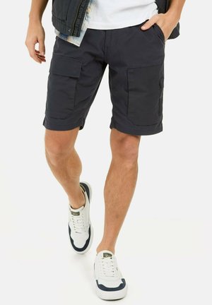 Navy cargo shorts with multiple pockets, flat front, and hemmed cuffs. Paired with white sneakers featuring navy accents.