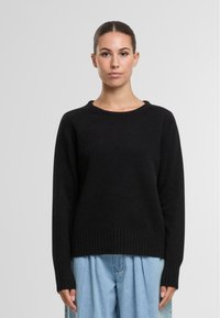 Schwarzer gestrickter Pullover mit Rundhalsausschnitt und gerippten Bündchen. Lässige Passform mit einer leicht verkürzten Länge, kombiniert mit hellblauen, lockeren Hosen.