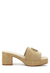 Mule in suede beige con platforma, punta rotonda, ampia fascia e un dettaglio dorato circolare sulla parte anteriore. Tacco a blocco con finitura testurizzata.