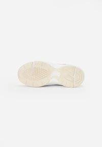 Sneaker sole with a light beige rubber pattern, featuring a textured grip and distinctive tread design for traction and stability.