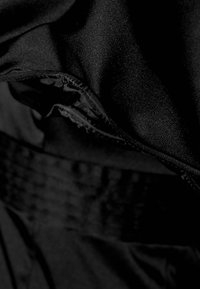 Tessuto nero con una texture liscia e una leggera lucentezza. Presenta una zip nascosta e una cintura strutturata. La prospettiva ravvicinata mette in evidenza i dettagli.