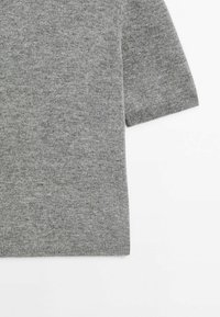 Pull en maille gris à manches courtes avec un tissu doux et texturé et des poignets côtelés, posé à plat sur un fond blanc.