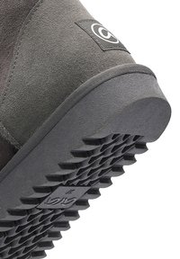 Primo piano del tallone di una scarpa in camoscio grigio con suola in gomma testurizzata e patch con logo cucito sul retro.