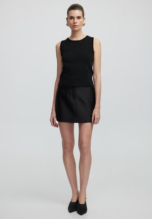 Top negro sin mangas hecho de tela texturizada, combinado con una falda corta negra de cintura alta. Calzado: tacones negros de punta. Diseño simple.