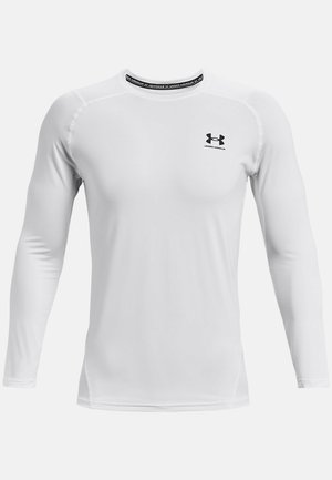 Chemise de sport à manches longues blanches en tissu lisse. Elle présente un col rond et un logo noir à l'avant. Les coutures mettent en valeur le design.