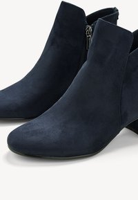 Bottines en daim bleu marine avec fermeture éclair latérale et petit talon carré, vues de face et de profil sur fond blanc.