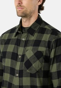 Groene en zwarte geruite shirt gemaakt van katoen, met een knoopsluiting aan de voorkant, een puntige kraag en een zak op de linkerkant van de borst.