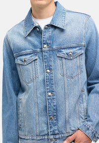 Lichtblauwe denimjas met een klassiek ontwerp, knoopsluitingen, twee borstzakken en een gestructureerde pasvorm. Zachte textuur en stevig materiaal.