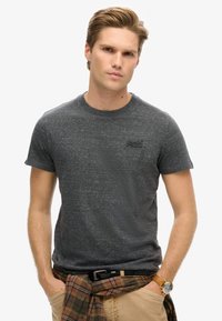 Mørkegrå crew-neck t-shirt lavet af struktureret stof, med korte ærmer og et lille sort logo på brystet. Parret med khaki bukser.