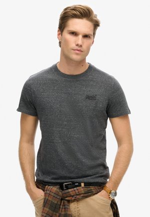 Donkergrijs t-shirt met ronde hals, gemaakt van een gestructureerde stof, met korte mouwen en een klein zwart logo op de borst. Gepaard met khaki broeken.