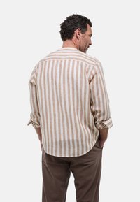 Chemise légère rayée en beige et blanc, avec une coupe décontractée, des manches retroussées et un ourlet arrondi. Tissu en lin texturé.