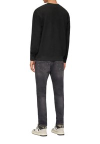 Zwarte, structuur sweatshirt met lange mouwen, gecombineerd met donkergrijze jeans. Schoenen hebben witte en zwarte accenten met veters.