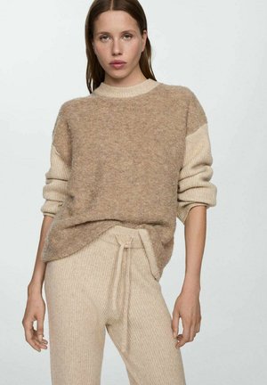 Beige knitted sweater with a soft texture and ribbed cuffs, paired with matching tapered pants featuring a drawstring waist.