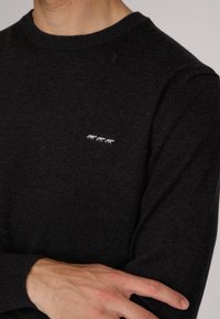 Pull tricot gris foncé avec un col rond. Présente trois petits motifs d'animaux blancs sur la poitrine. Manches et ourlet côtelés. Texture douce.