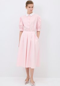 Abito rosa chiaro con un corpetto a colletto e bottoni, gonna plissettata, maniche corte a sbuffo e una texture liscia, accessorioso con scarpe metalliche.